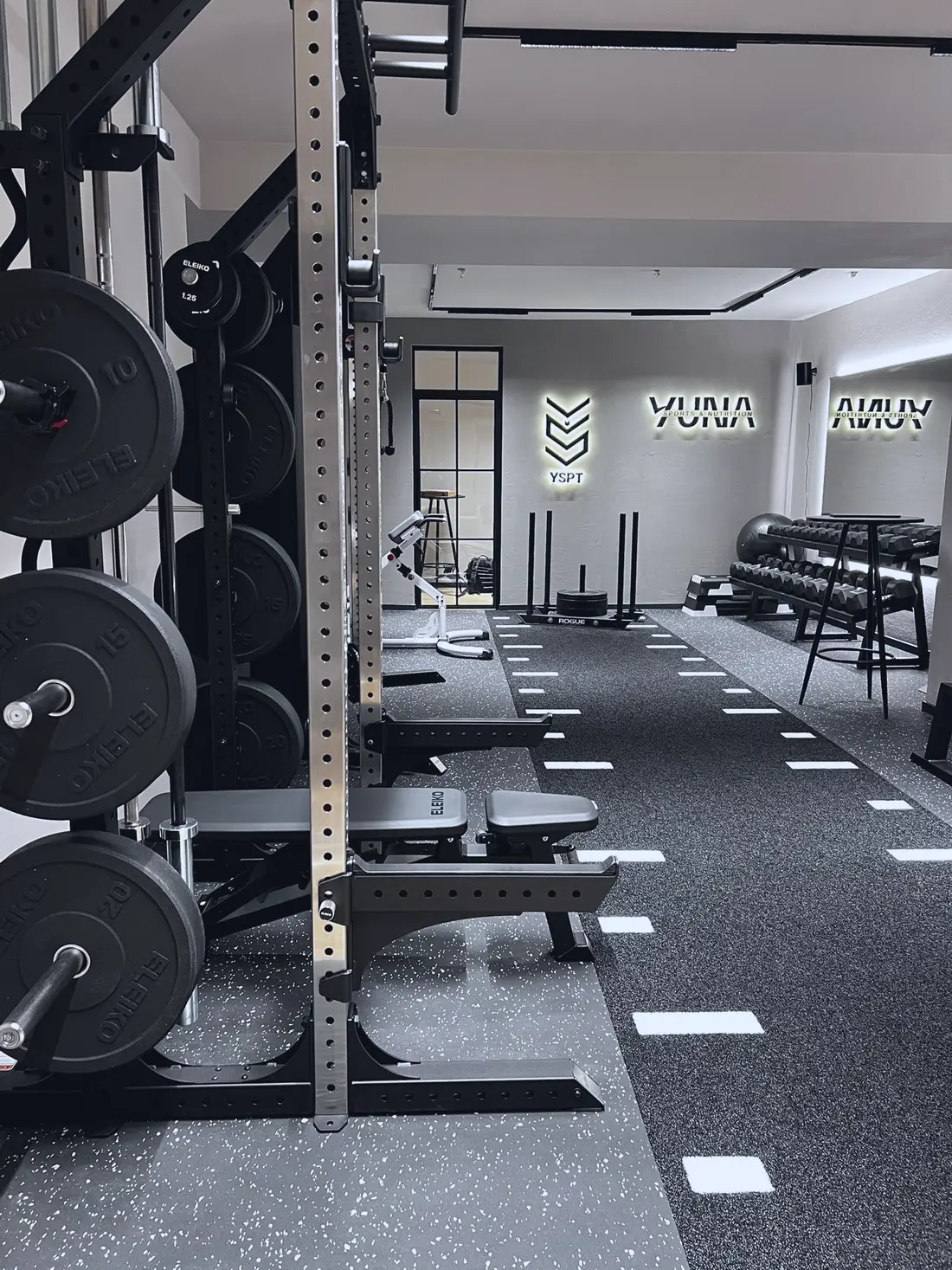 Blick ins YUNA Studio: Rack mit Hantelscheiben, freie Trainingsfläche und beleuchtete Logos